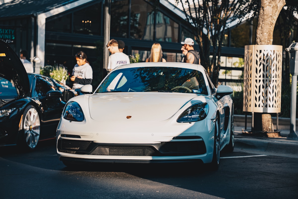 Une Porsche blanche garée devant un bâtiment avec des personnes.