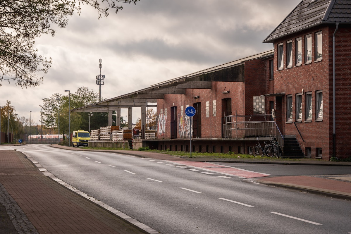Bâtiment industriel en briques, route, vélos, camion, ciel nuageux.