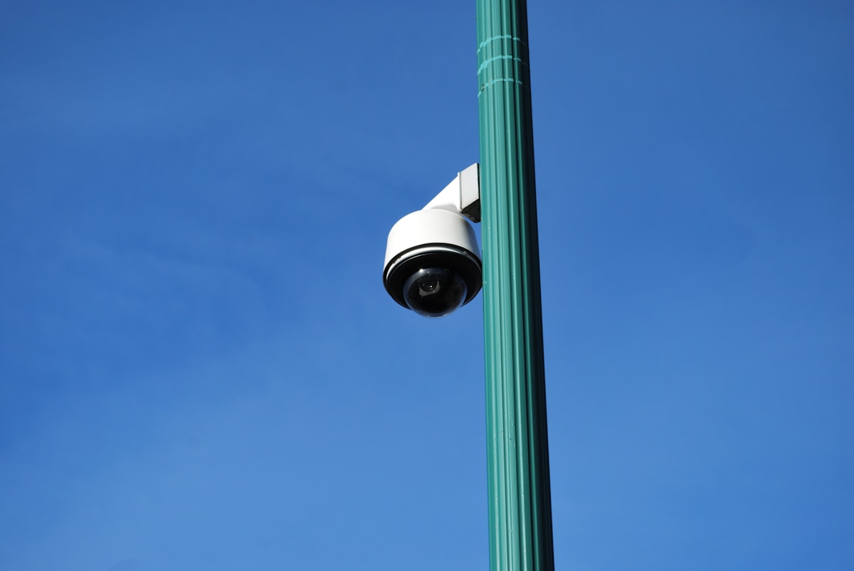 Caméra de surveillance montée sur un poteau contre un ciel bleu.