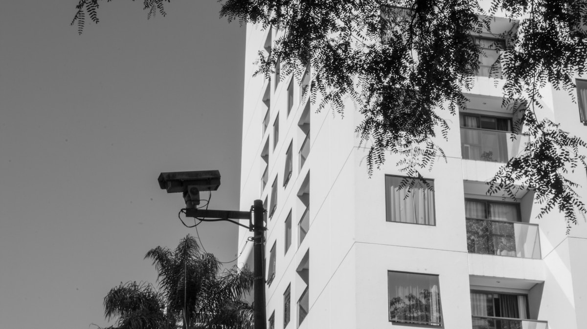 Bâtiment moderne avec caméra de surveillance, arbres et ombres.