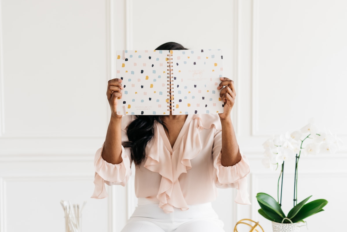 Femme tenant un cahier à motifs colorés devant son visage.