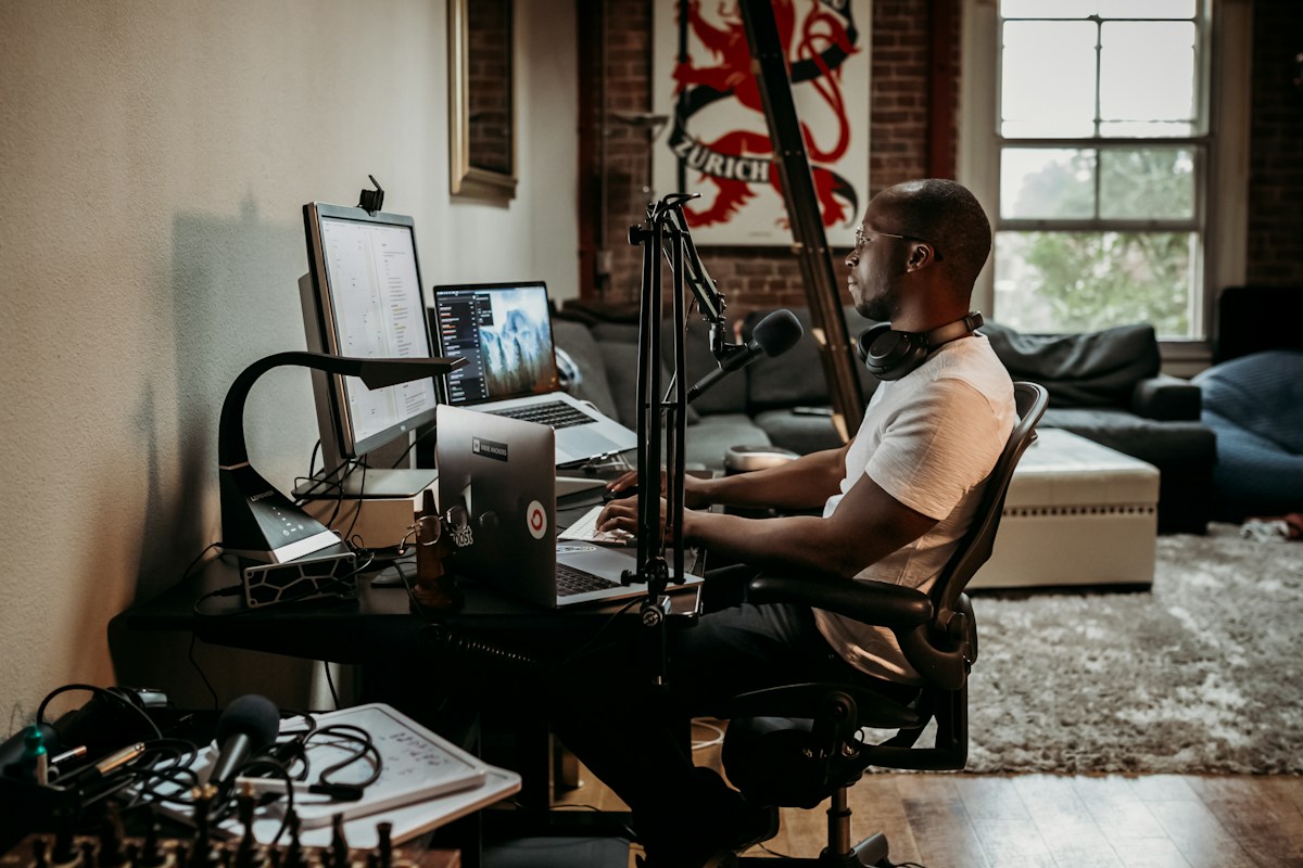 Homme noir travaillant devant un ordinateur avec microphone de podcast.