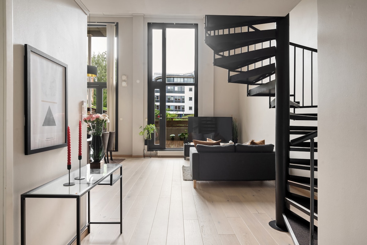 Intérieur moderne avec escalier en colimaçon, canapé et fenêtre panoramique.