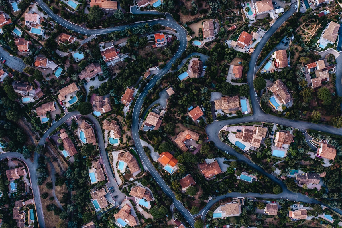 Vue aérienne d'un village méditerranéen avec maisons, piscines et routes sinueuses.