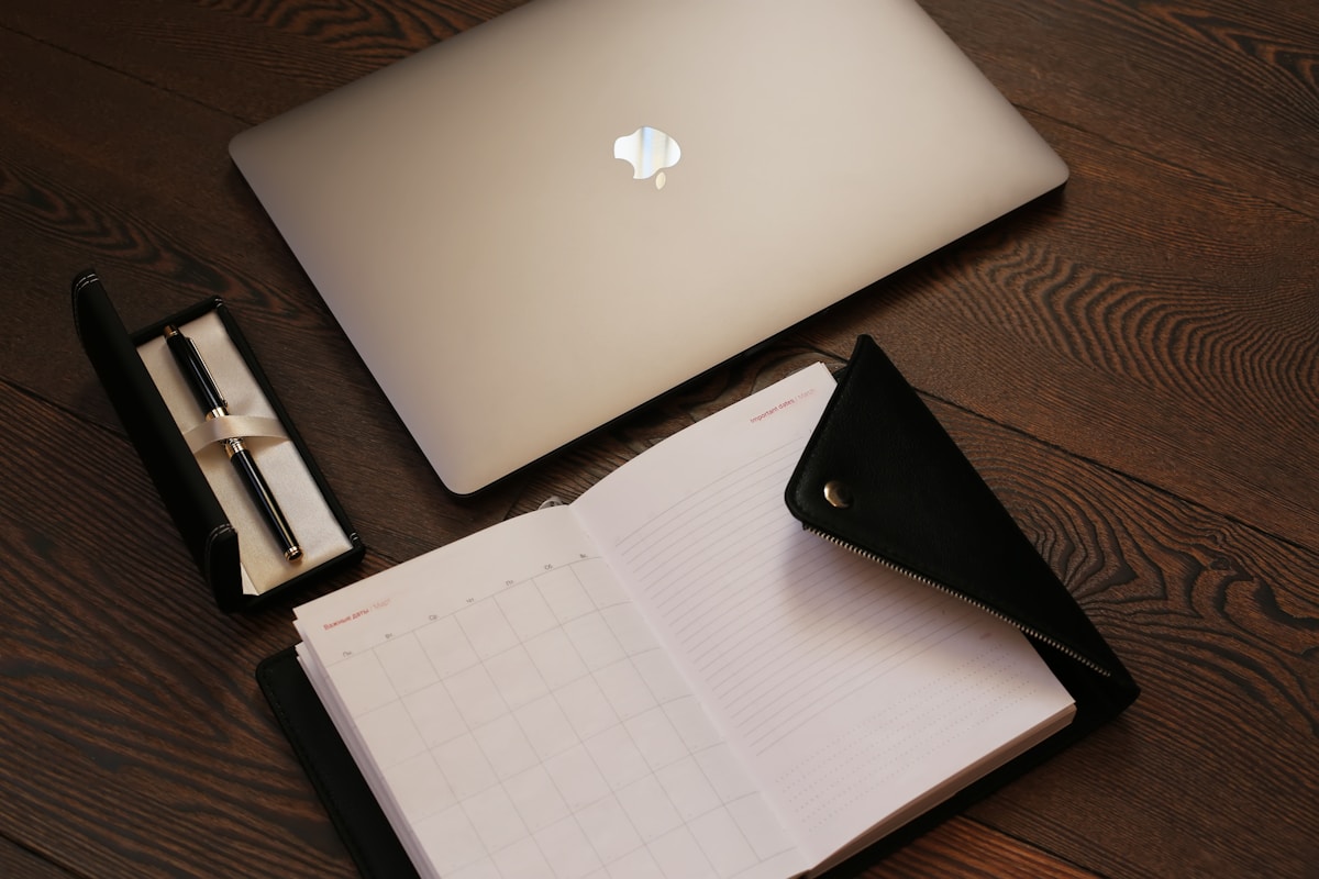 Ordinateur portable, cahier, stylo sur une table en bois.