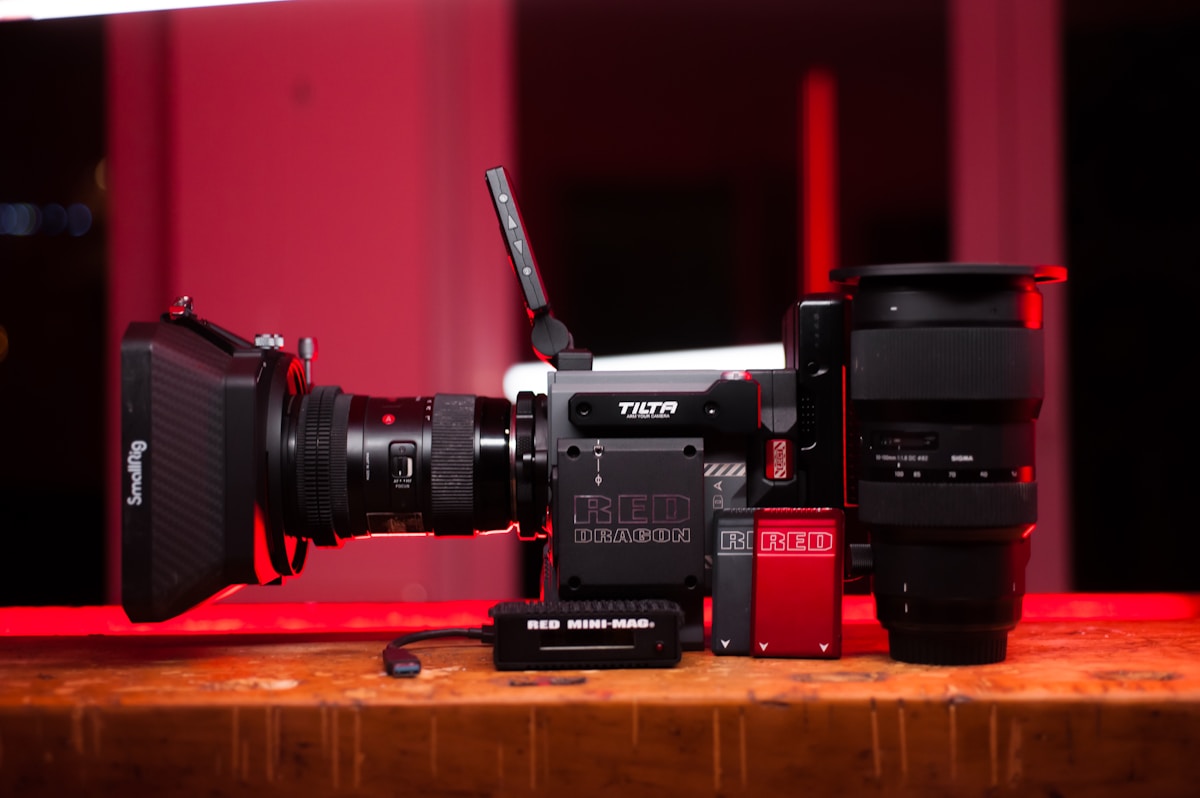 Caméra RED Dragon avec objectif et accessoires sur fond rouge.