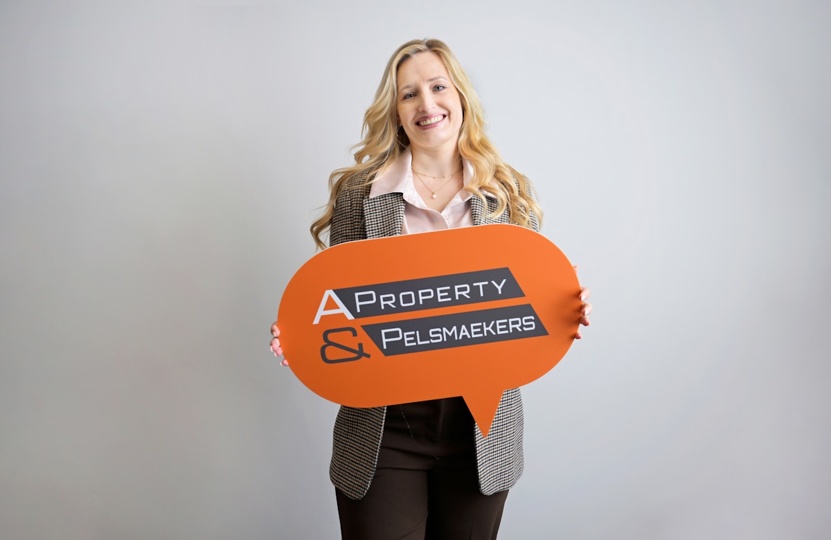 Femme souriante tenant une enseigne orange de l'entreprise immobilière.