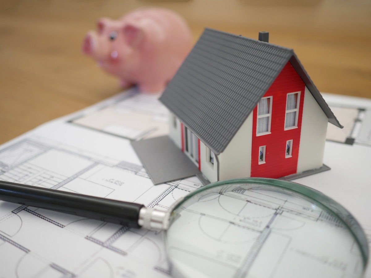 Maquette de maison rouge sur des plans architecturaux avec loupe.