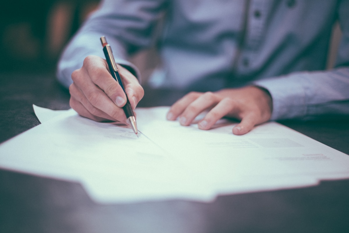 Mains d'une personne écrivant sur un document avec un stylo.
