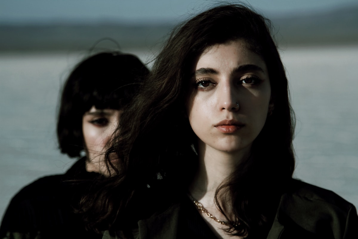 Deux jeunes femmes aux regards intenses et pénétrants, dans une atmosphère sombre et mystérieuse.