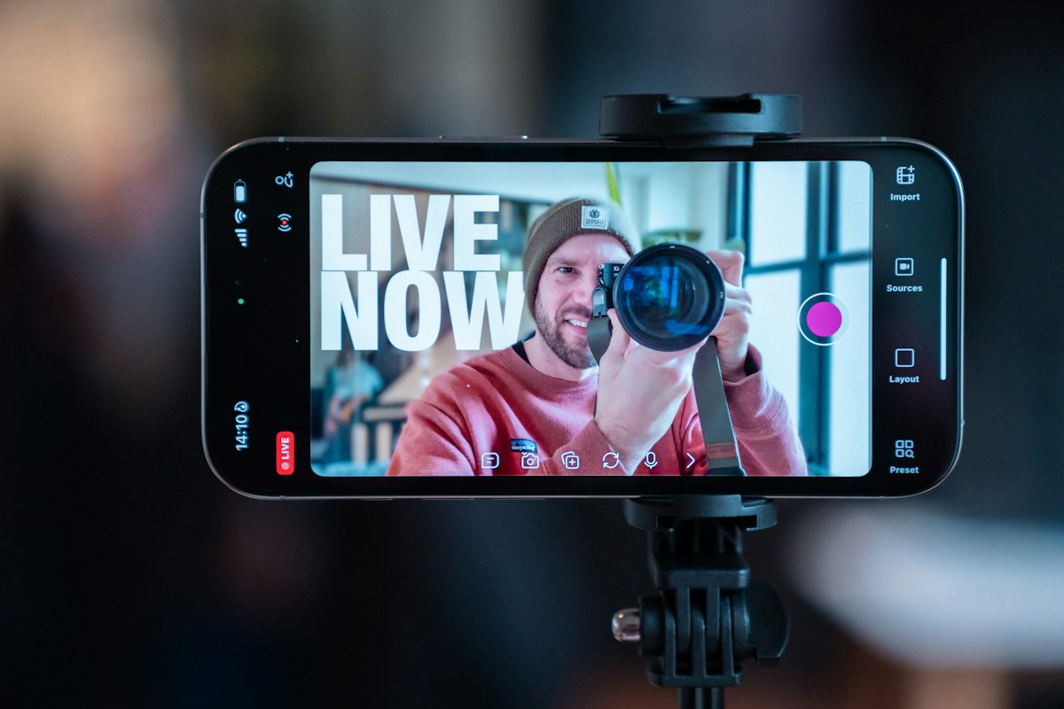 Smartphone sur trépied filmant un photographe avec texte « LIVE NOW »