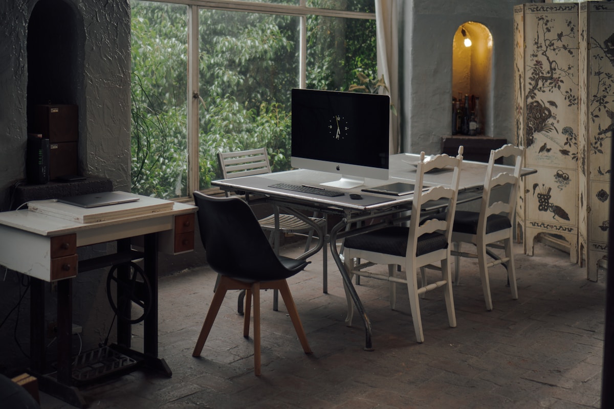 Bureau de travail dans un intérieur rustique avec ordinateur, chaises et fenêtre sur la nature.