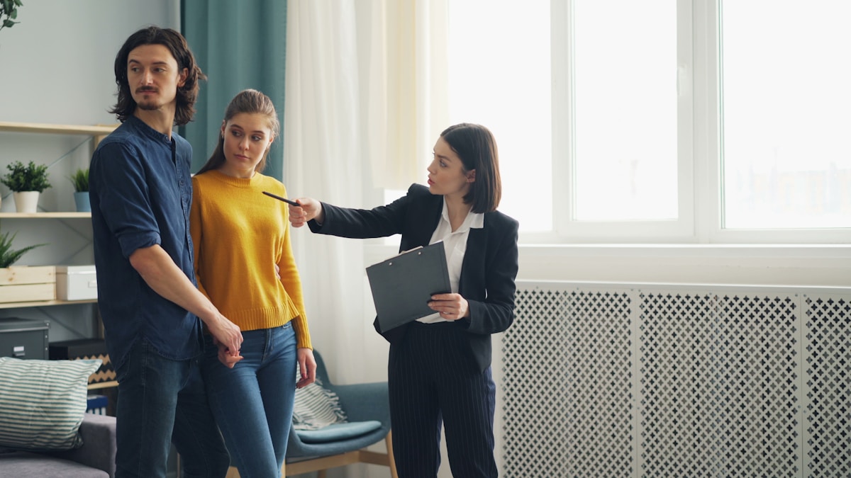 Trois personnes dans un bureau, une femme en costume interroge un couple.