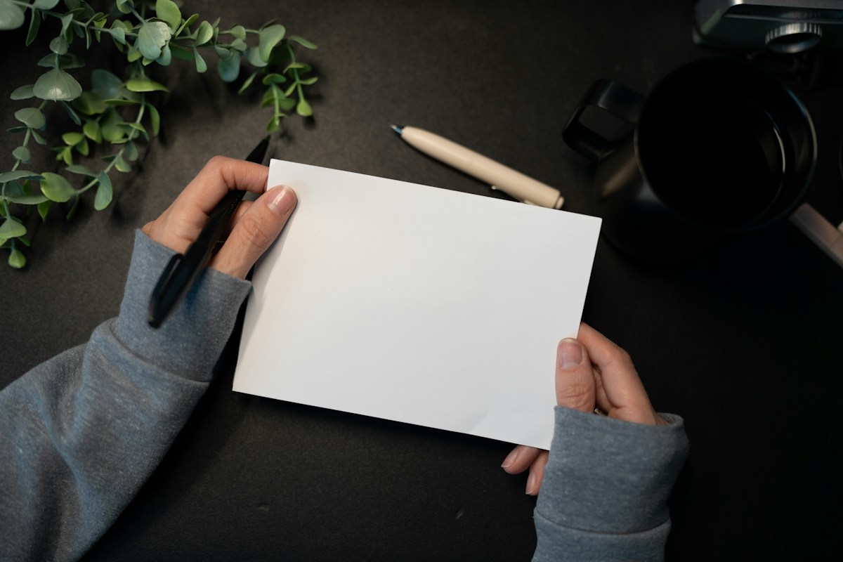 Mains tenant une feuille blanche et un stylo noir sur bureau sombre