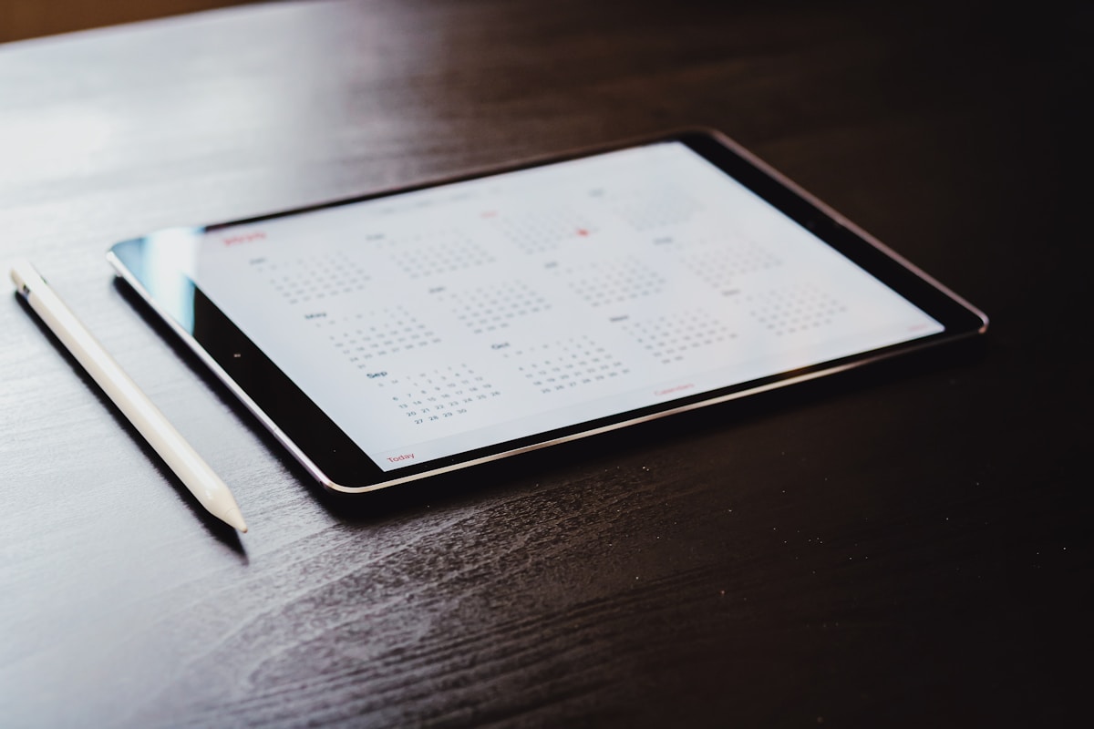 Tablette numérique affichant un calendrier sur un bureau sombre.