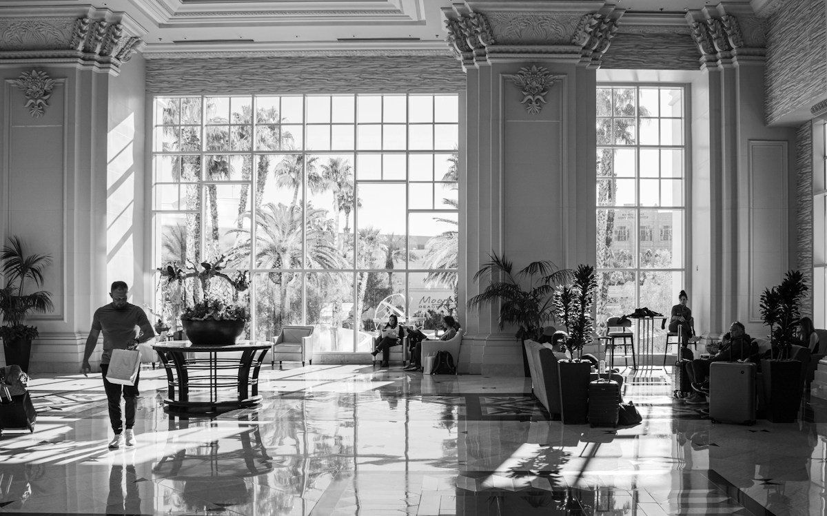 Hall d’hôtel luxueux baigné de lumière, palmiers et voyageurs assis