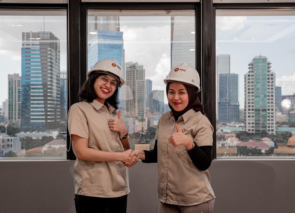 Deux femmes en uniforme de construction se serrant la main devant un paysage urbain.