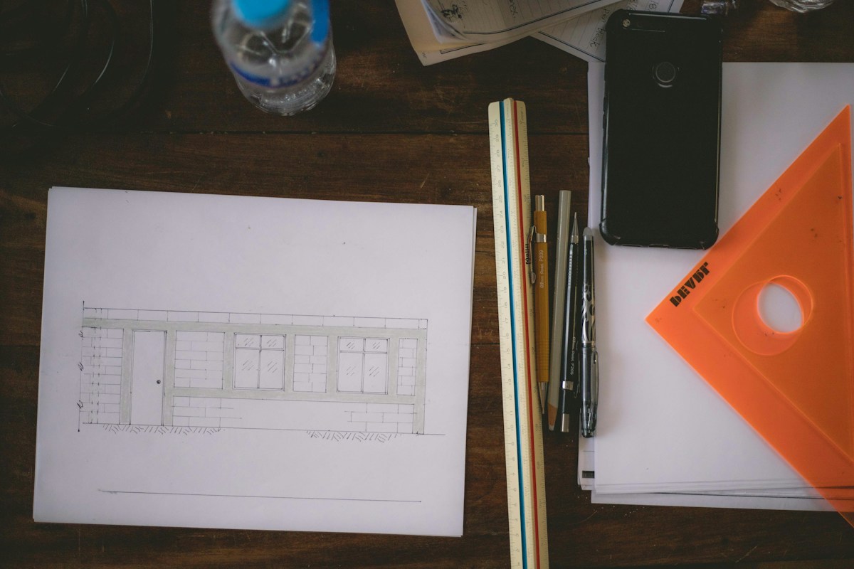 Plan architectural dessiné, règle, stylos et équerre orange.