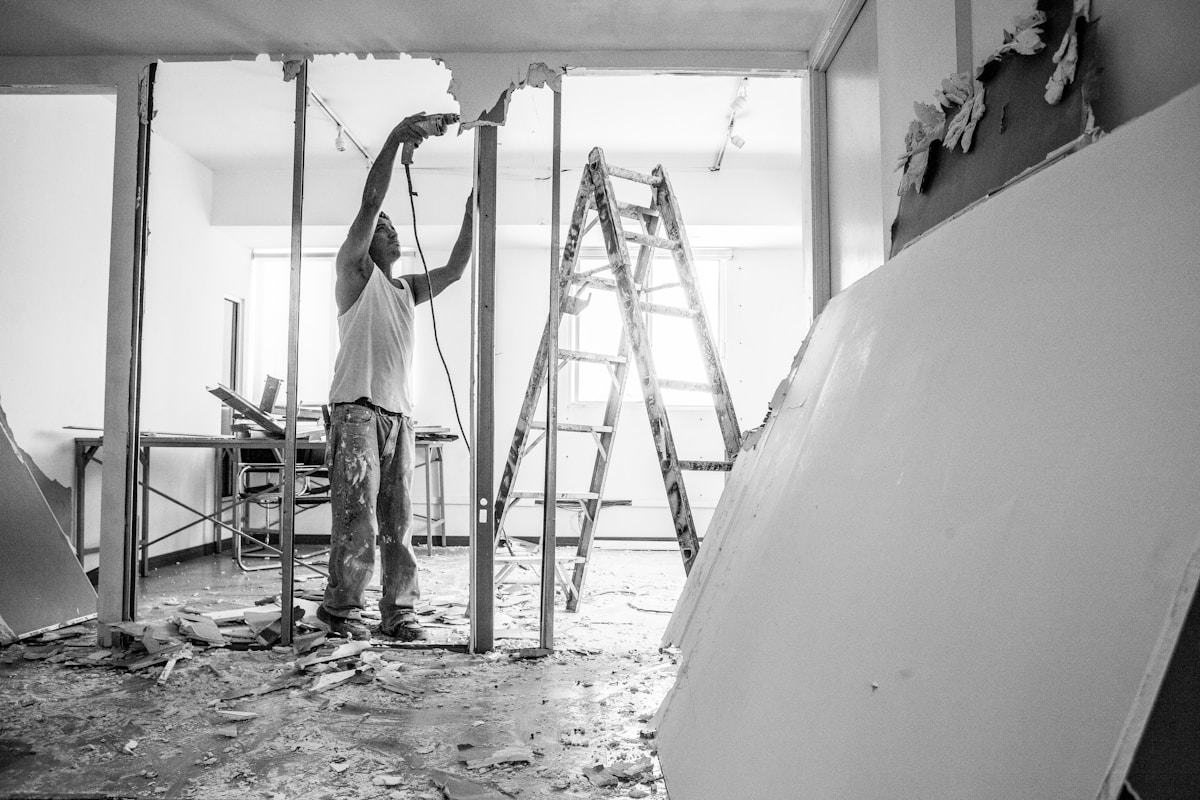 Travaux de rénovation, homme sur une échelle, débris au sol.