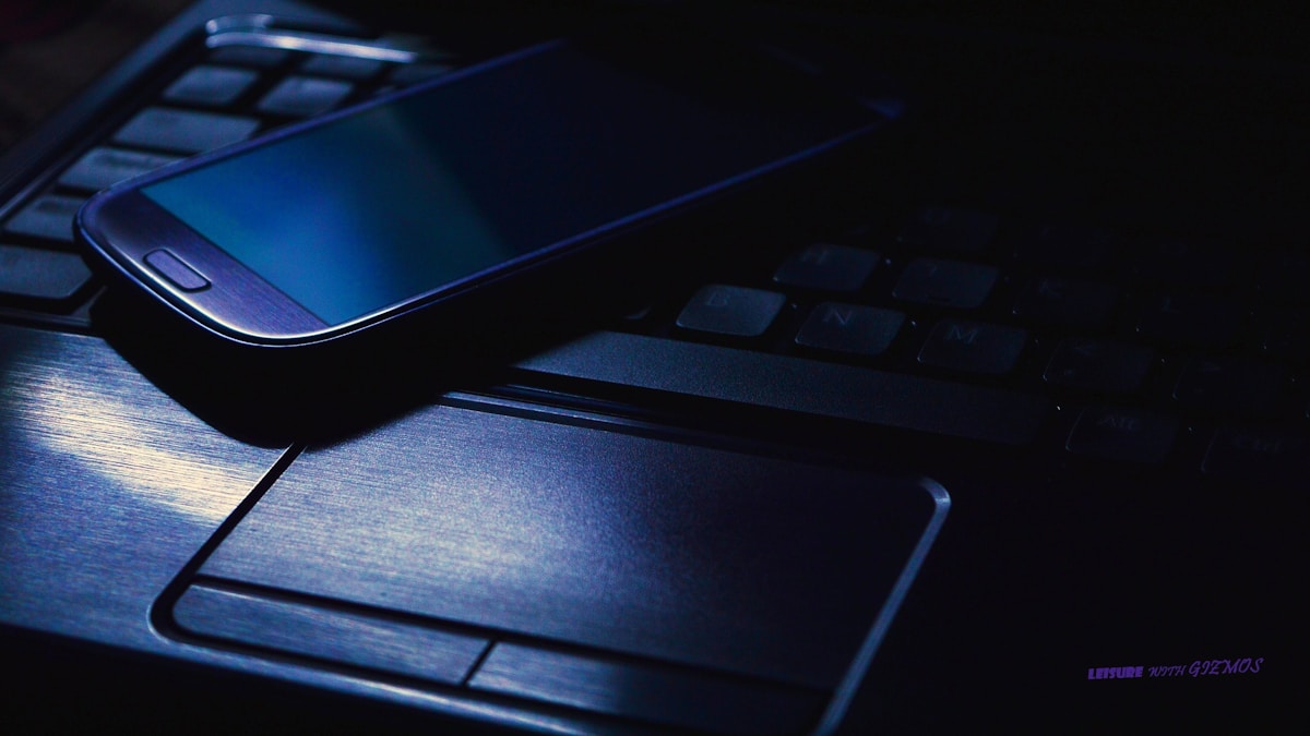 Clavier d'ordinateur, souris et smartphone bleu foncé sur un bureau sombre.