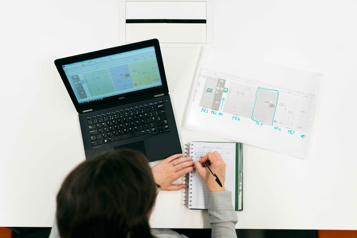 Ordinateur portable, cahier, plans, stylo, mains d'une personne travaillant.