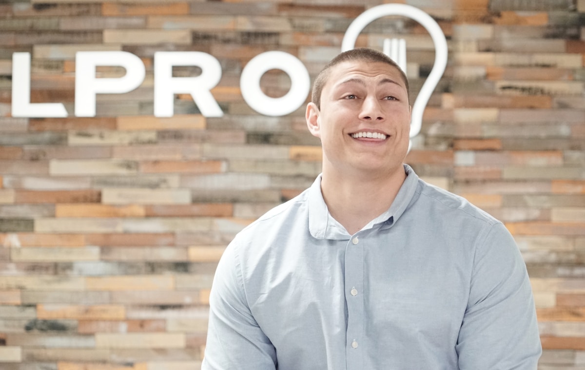 Homme souriant devant un mur de briques avec le mot "LPRO".
