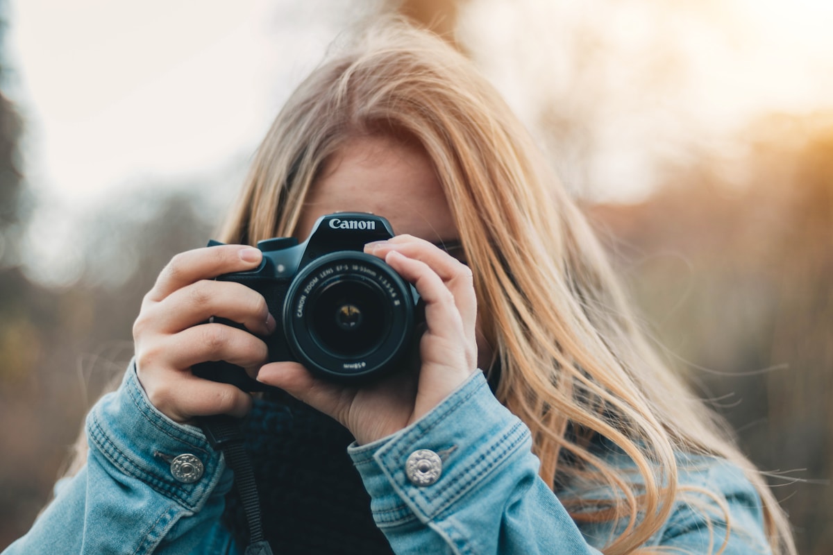 Femme photographiant avec un appareil photo Canon dans un paysage flou.