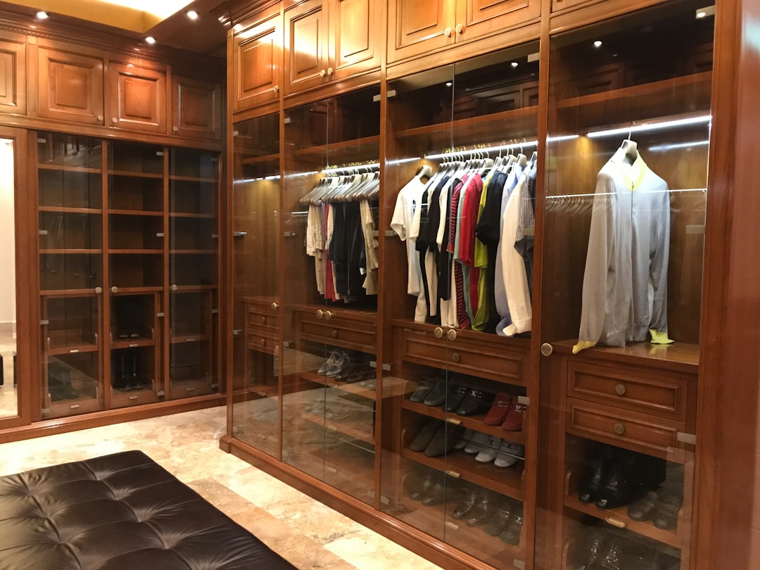 prix dressing sur mesure - A beautifully organized custom walk-in closet with warm wood shelving, integrated lighting, and ne