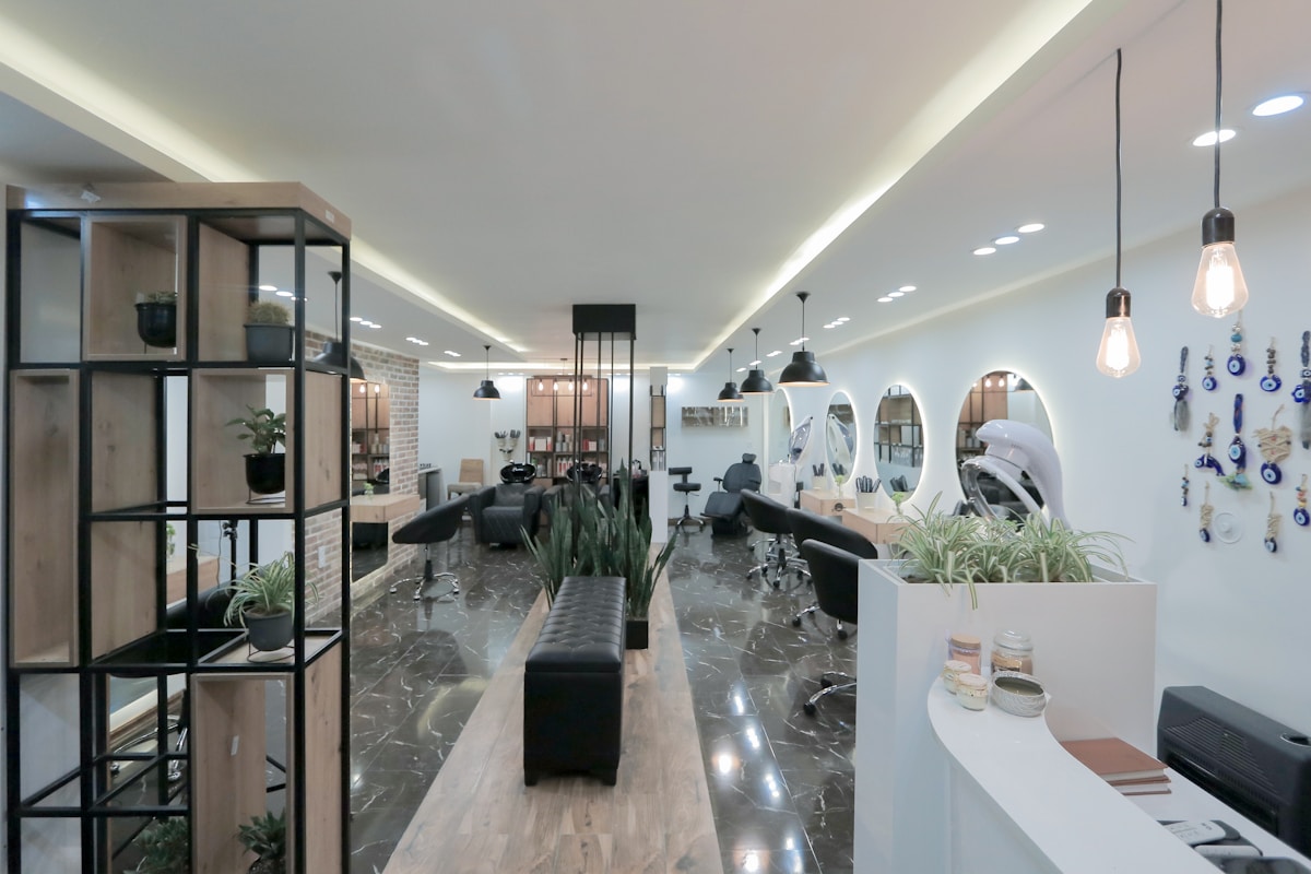 Salon de coiffure moderne avec étagères, miroirs et plantes décoratives.