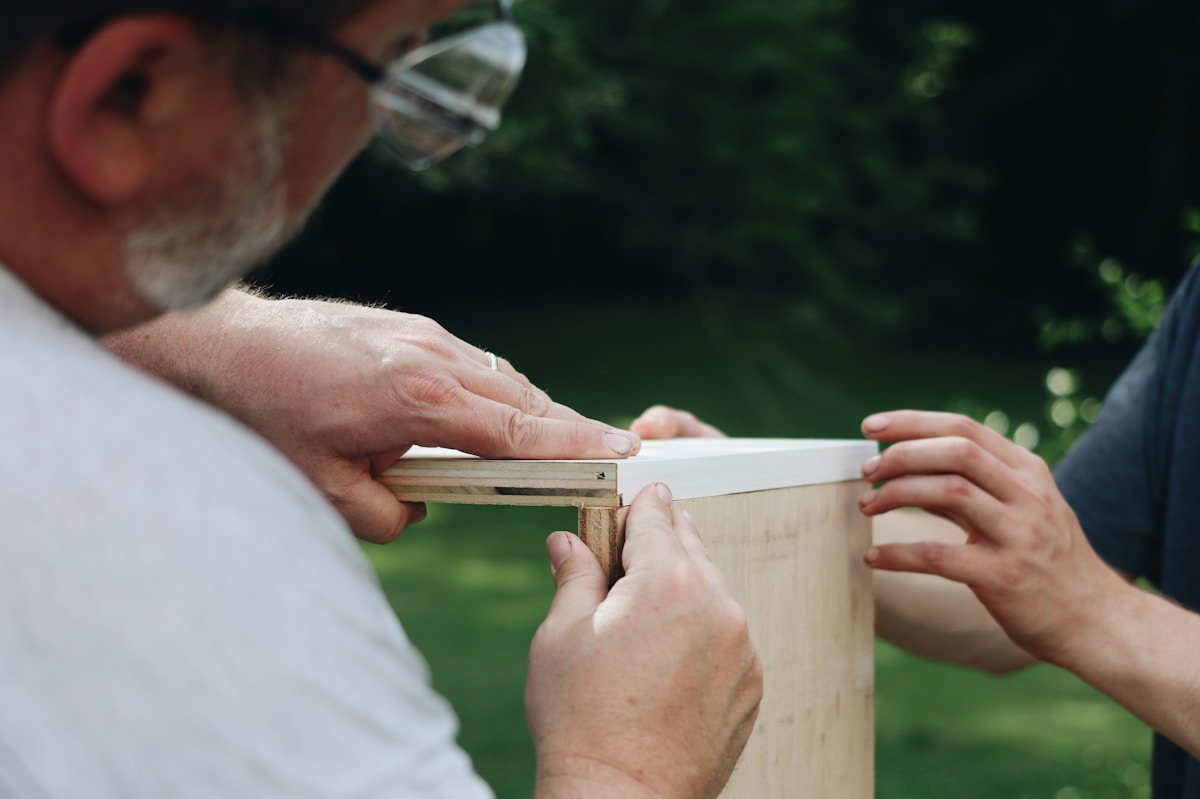 Deux mains assemblant une structure en bois à l'extérieur.