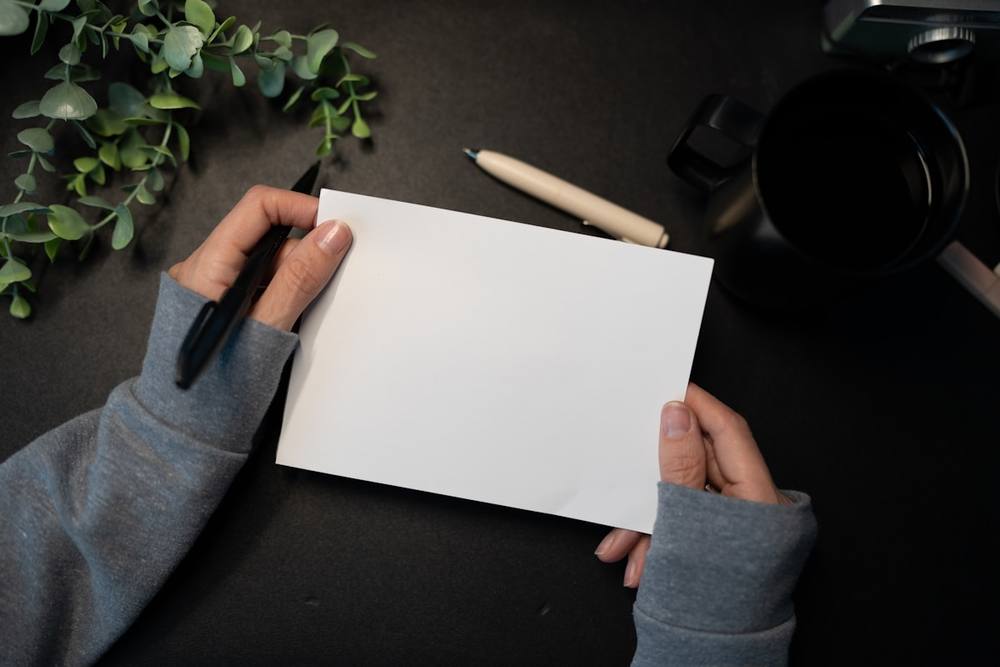 Mains tenant une carte vierge avec un stylo et une plante.