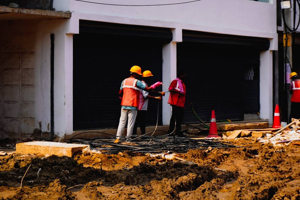 Trois travailleurs en uniforme réparant le sol devant un bâtiment.
