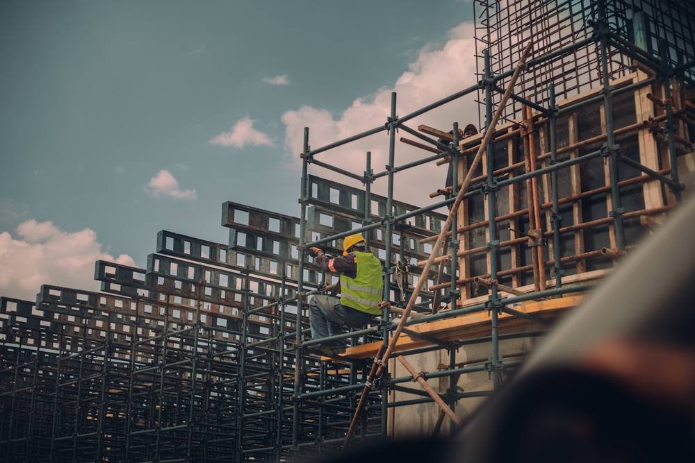 Chantier de construction avec échafaudage et ouvrier en gilet de sécurité.