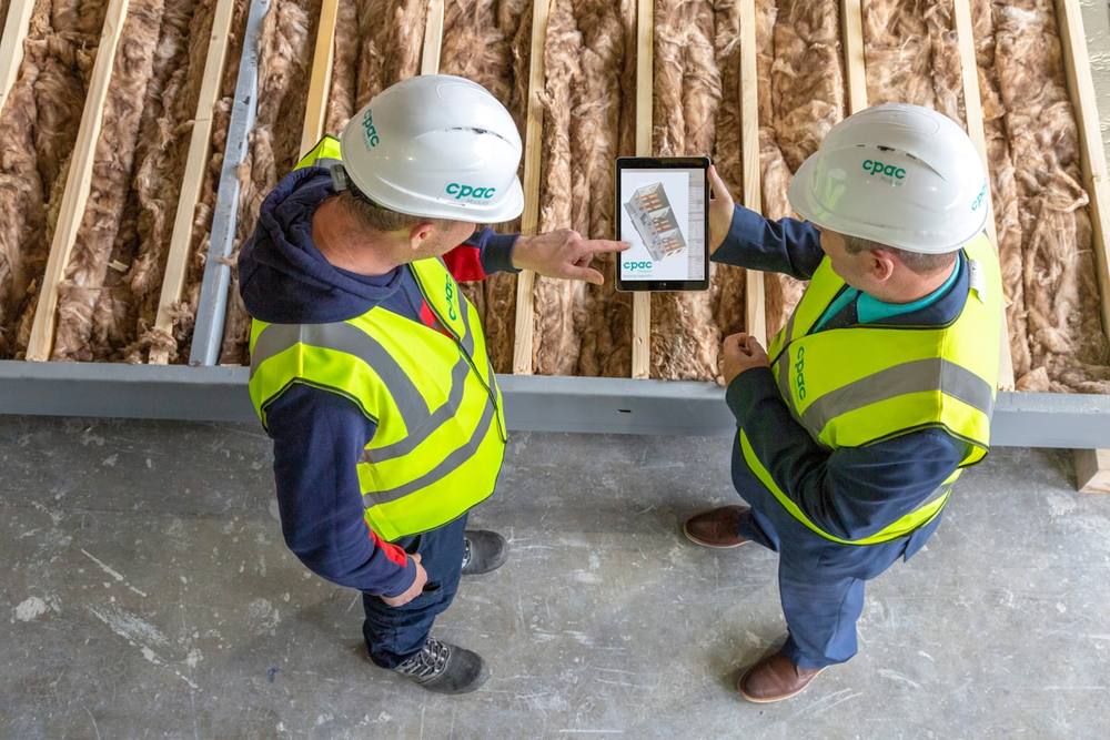 Deux travailleurs du bâtiment en tenue de sécurité examinent une tablette numérique sur un chantier.