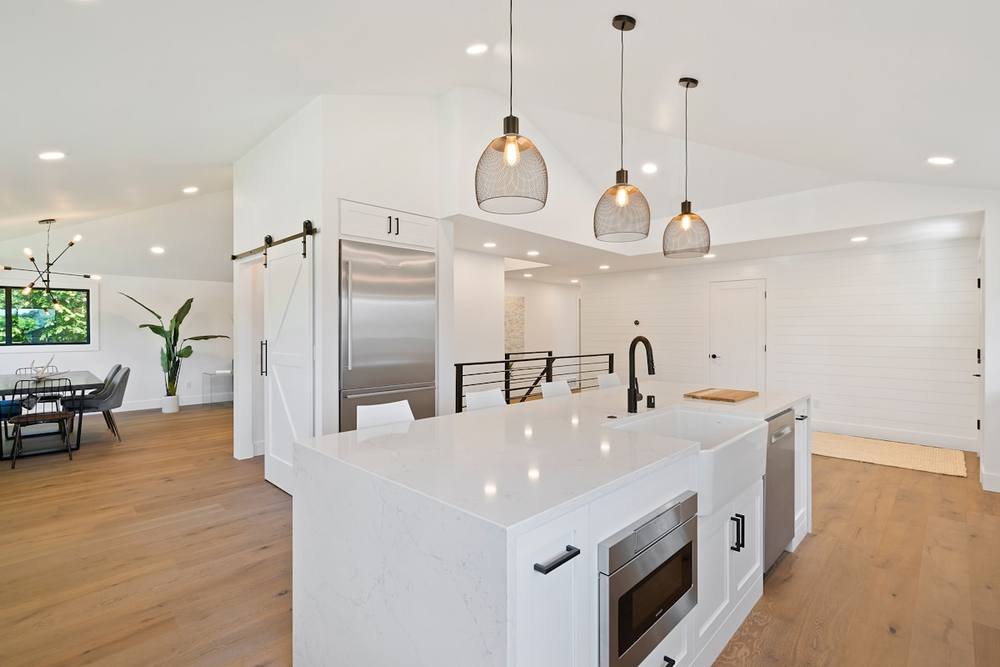 Cuisine moderne avec îlot central, luminaires suspendus et réfrigérateur en acier inoxydable.