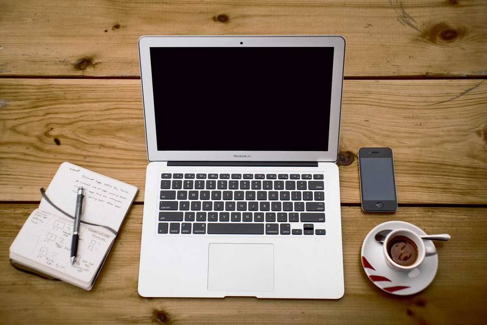 Un ordinateur portable, un téléphone, un cahier et un café sur une surface en bois.