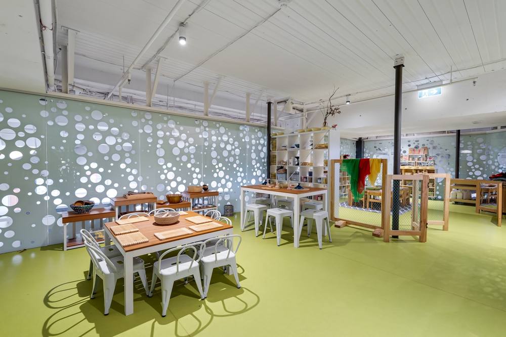 Salle de classe colorée avec tables, chaises et étagères.