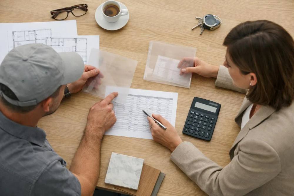 Propriétaire examinant le contrat de rénovation et le budget avec l'entrepreneur dans une villa genevoise moderne, documents de tarification transparents et calculatrice visibles sur la table, atmosphère de consultation professionnelle.