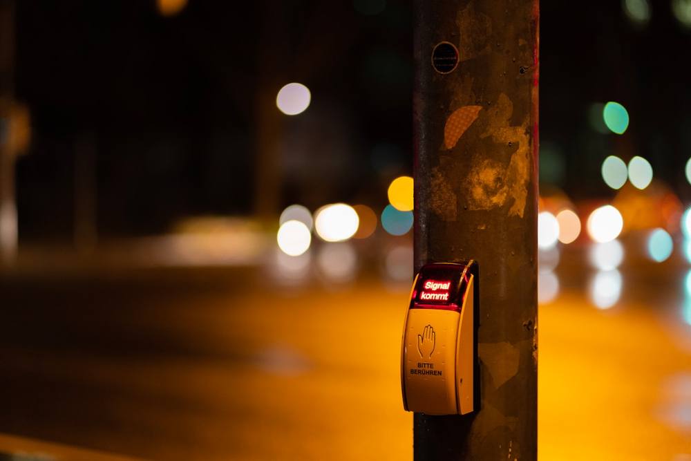 Bouton de traversée piétonne la nuit, avec des lumières de rue floues en arrière-plan.