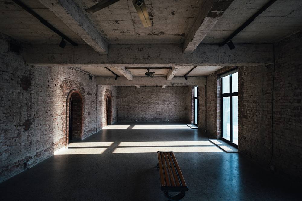 Salle de brique industrielle abandonnée avec fenêtres et banc en bois.