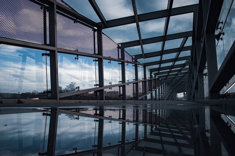 Passerelle vitrée réfléchissant le ciel nuageux.