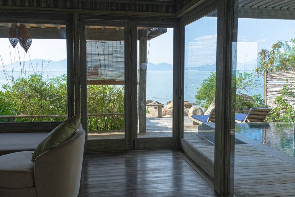 Intérieur d'un bungalow avec vue panoramique sur la mer et la végétation.