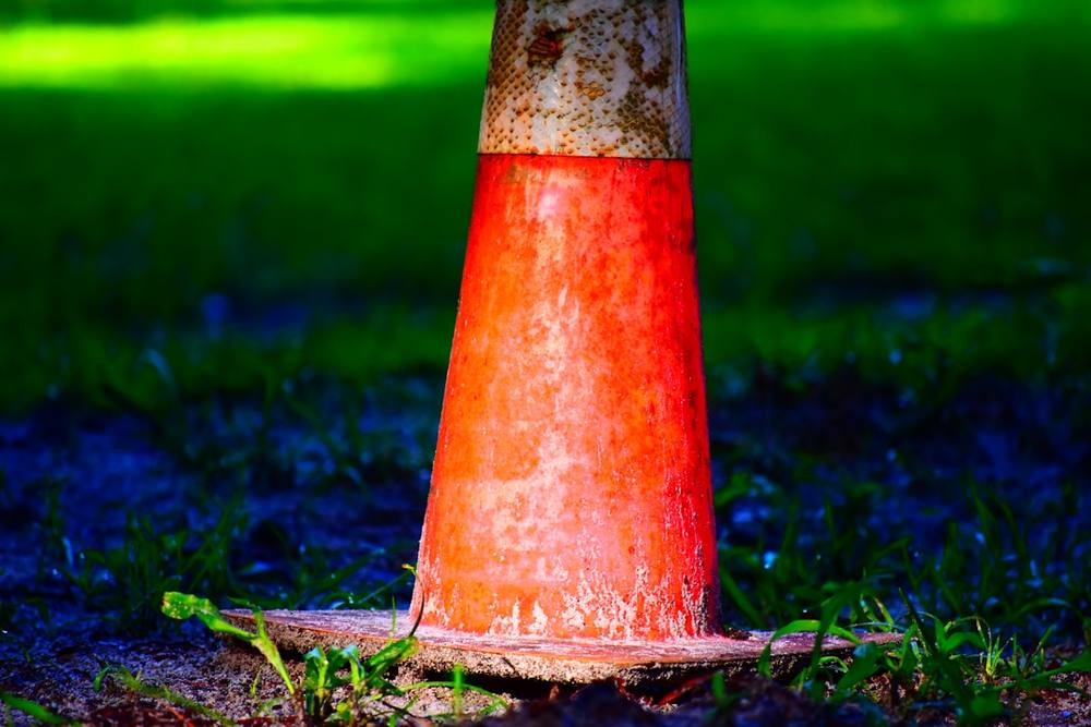 Cône de signalisation rouge et rouillé sur l'herbe verte.