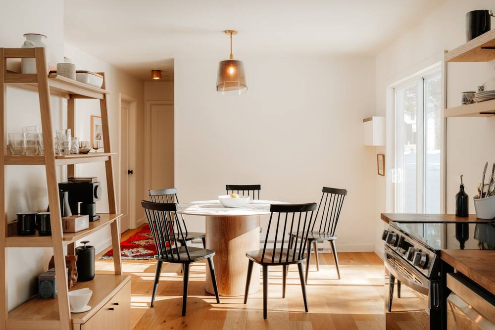 Salle à manger moderne avec table ronde, chaises noires et étagères en bois.