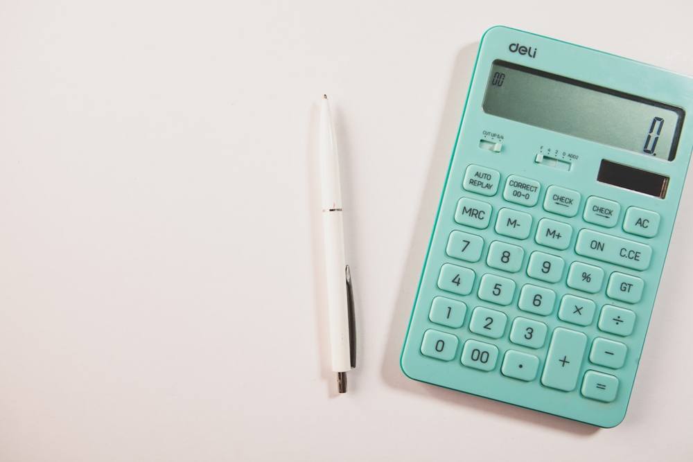 Calculatrice de bureau de couleur turquoise et stylo blanc sur fond blanc.