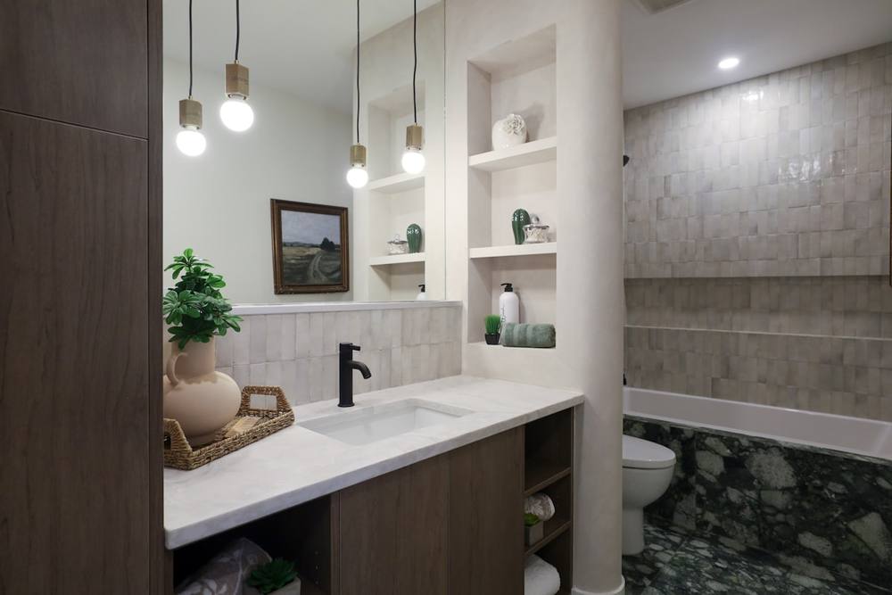 Salle de bain moderne avec étagères, lavabo et carrelage gris.