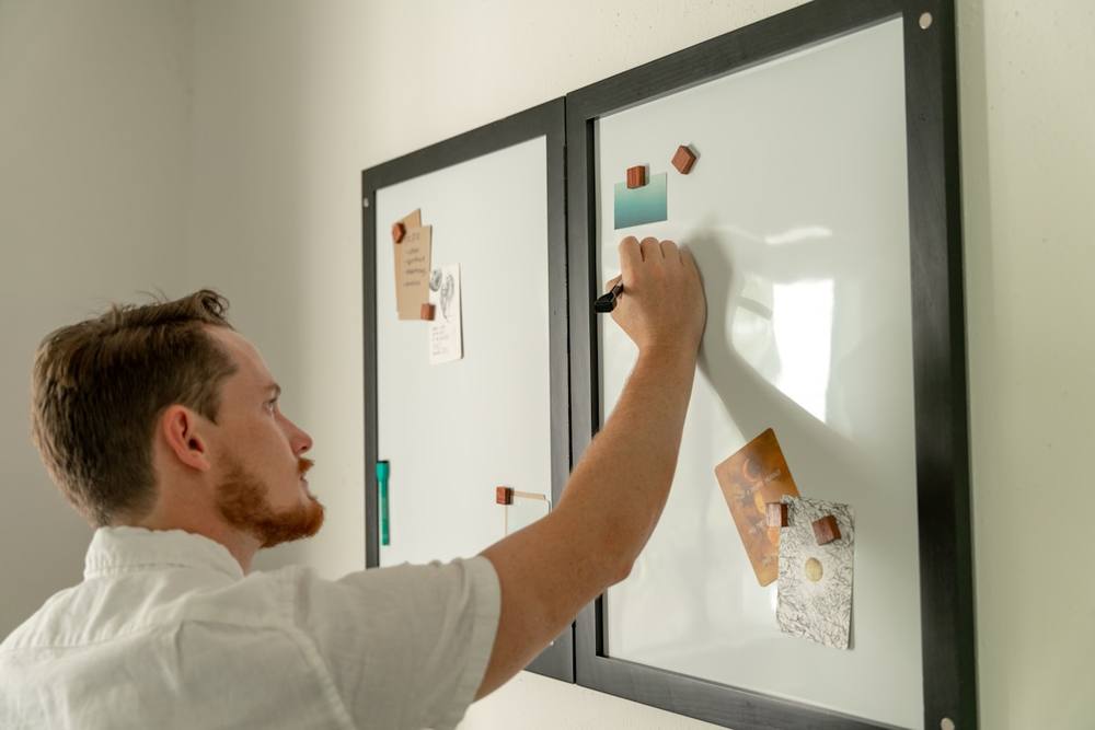 Un homme écrit sur un tableau blanc avec des notes autocollantes.