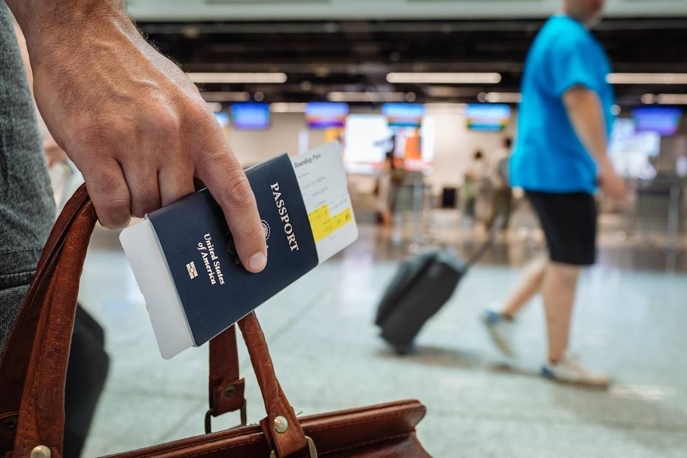 Passeport à la main dans un aéroport avec un voyageur en arrière-plan.