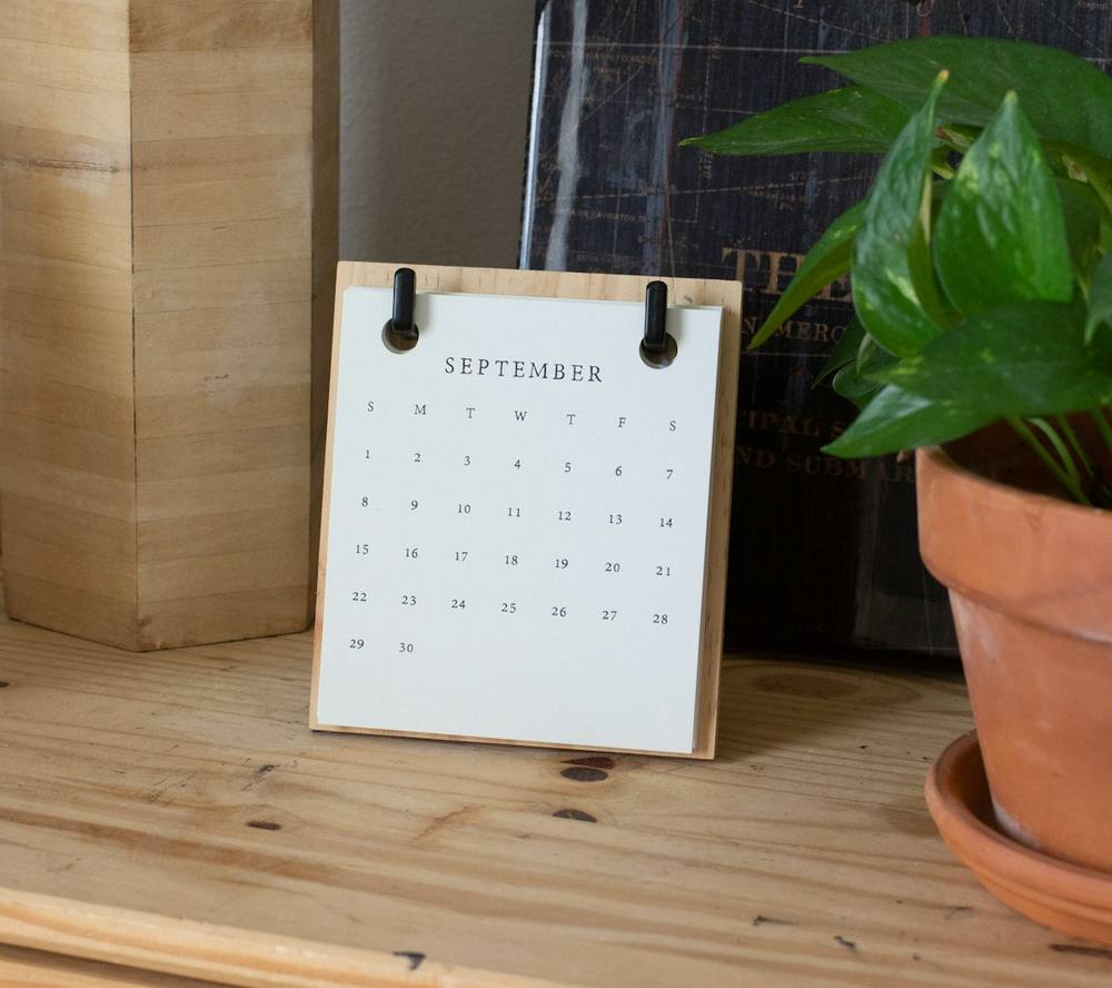 Calendrier de septembre sur un bureau en bois avec une plante en pot.