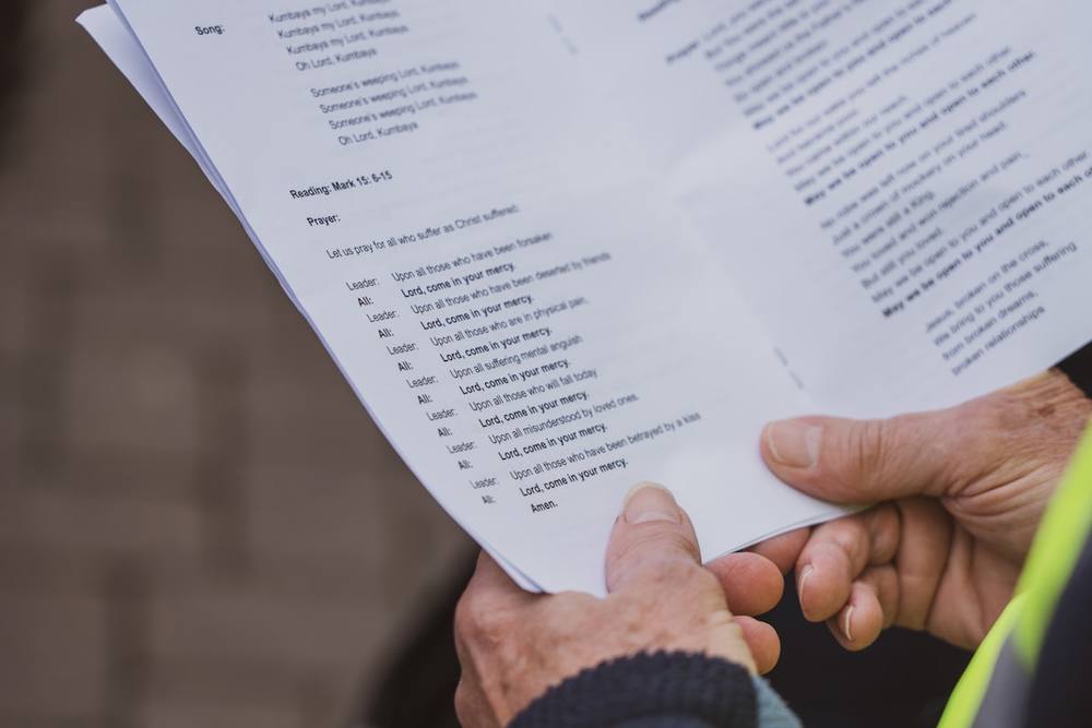 Feuille de prière avec texte et mains tenant le document.